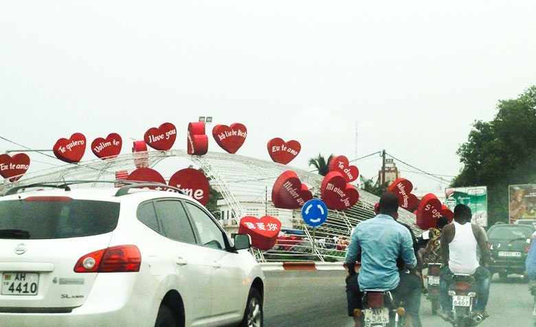 Auf einer Kuppel aus Stahl über einem Grünstreifen neben einer befahrenen Straße sind herzförmige Luftballons mit Übersetzungen von „Ich liebe Dich“ in vielen verschiedenen Sprachen angebracht.