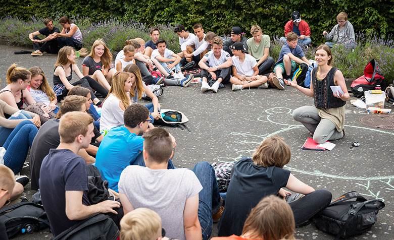Eine Gruppe junger Menschen sitzt in einem Kreis zusammen und hört einer Referentin zu.