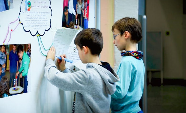 Zwei Jungs stehen an einer Whiteboard und schreiben etwas auf.