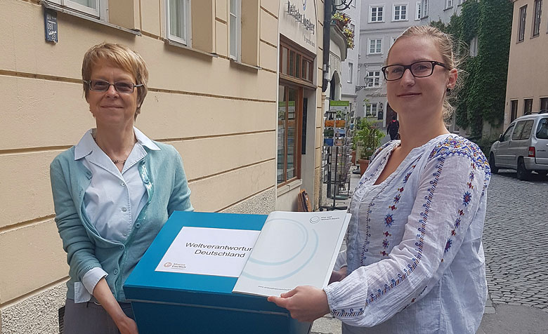 Die beiden Mitarbeiterinnen der Regionalen Bildungsstelle Bayern stehen mit einer Materialkiste auf der Straße vor ihrem Büro.