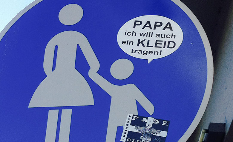 Auf ein Fußgängerinnen und Fußgänger Straßenschild wurde ein Sticker oberhalb des Kindes geklebt, auf dem steht: „Papa ich will auch ein Kleid tragen!“.