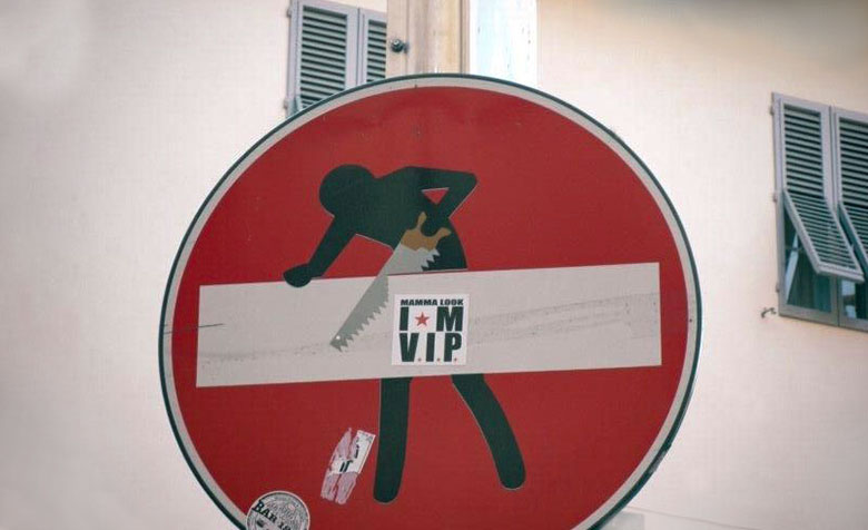 Auf ein Durchfahrt verboten Straßenschild wurde ein Figur geklebt, die mit einer Säge den Querbalken ansägt.
